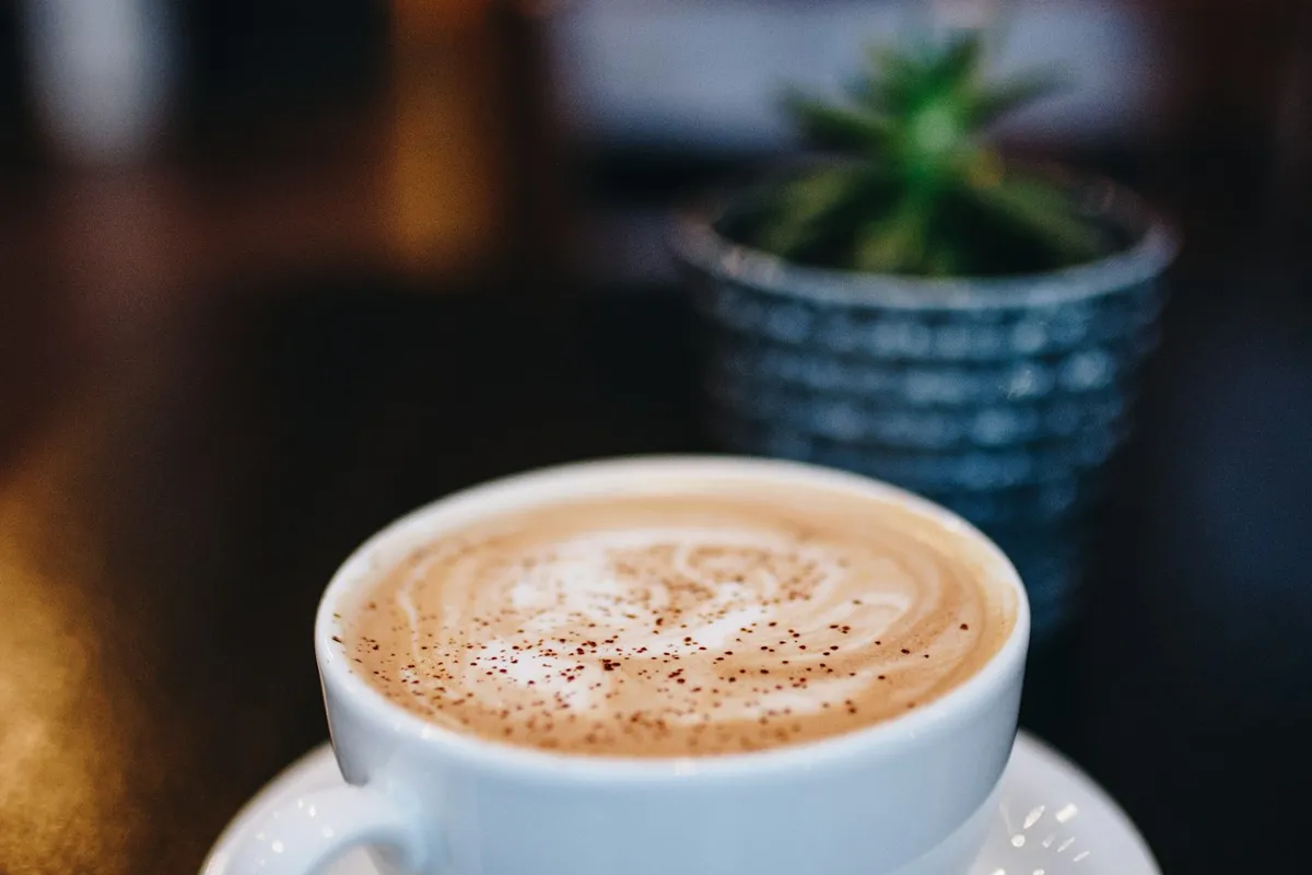 Xícara de café quente ao lado de cafeteira com jarra de vidro, ilustrando café coado na bancada