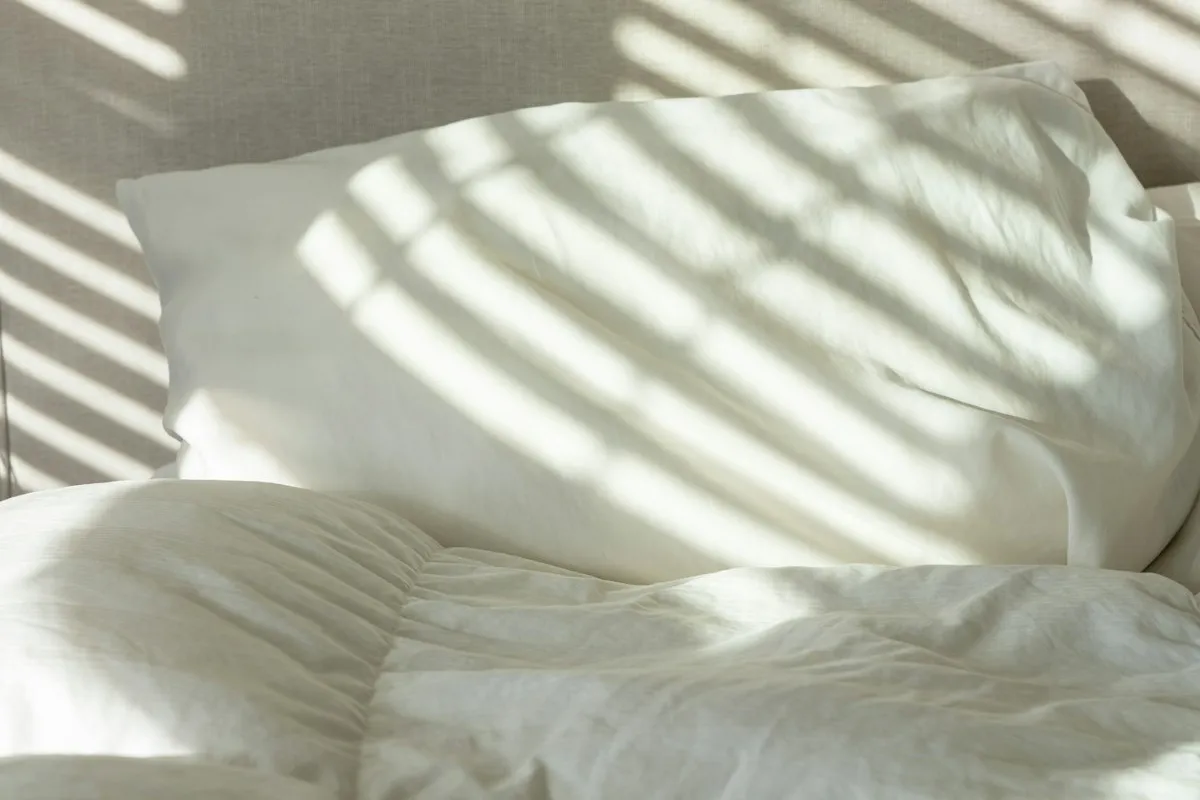 Cama de casal arrumada com lençol claro e travesseiros em quarto iluminado, ilustração da categoria de colchões, não é packshot da BF Colchões
