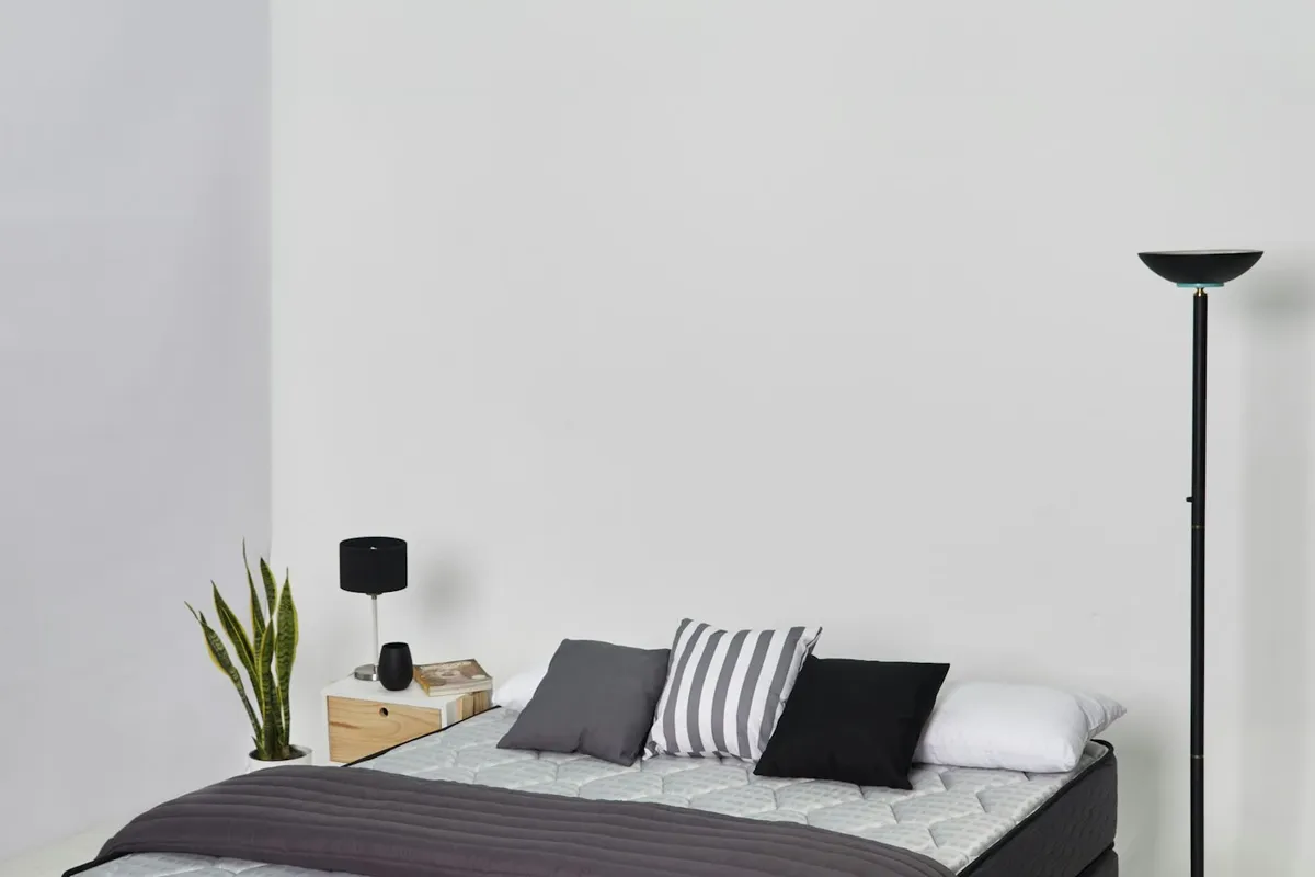 Cama moderna de casal com lençóis claros e almofadas, ilustrando colchão em quarto acolhedor