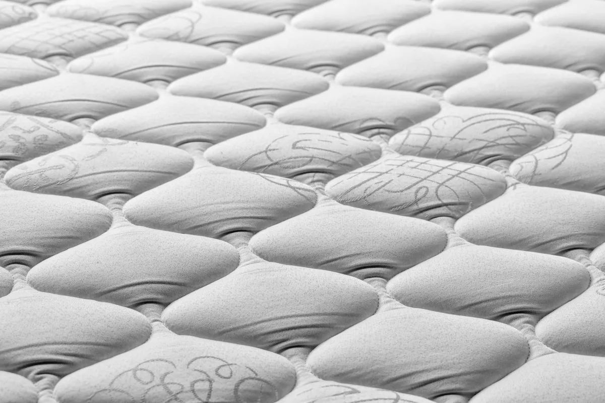 Cama de casal arrumada com colchão espesso e lençóis brancos, ilustrando colchão de alta densidade