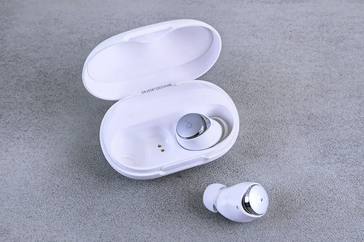Fones de ouvido sem fio brancos com estojo de recarga sobre bancada, ilustrando modelo TWS compacto